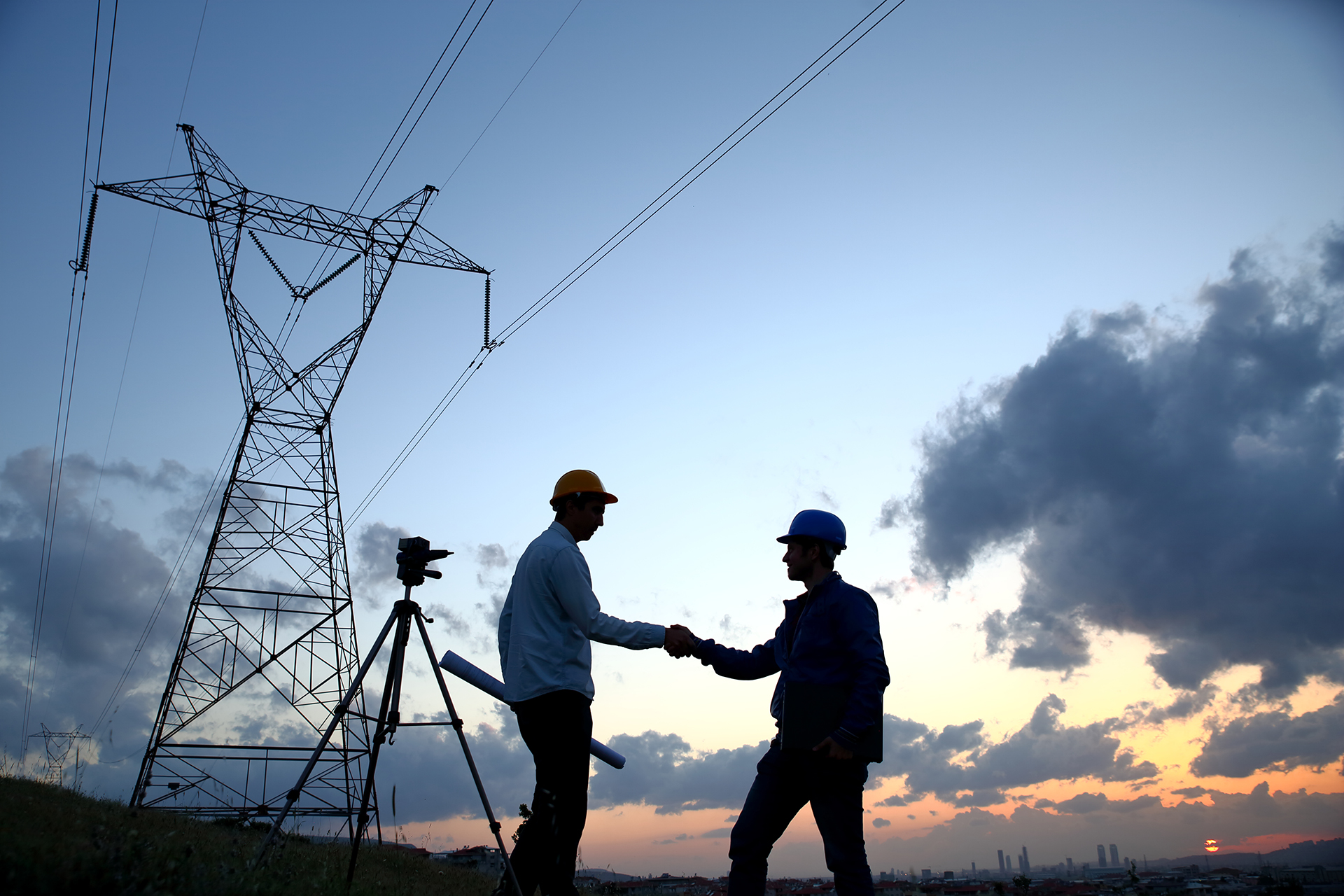 Two engineers shaking hands in front of a power line