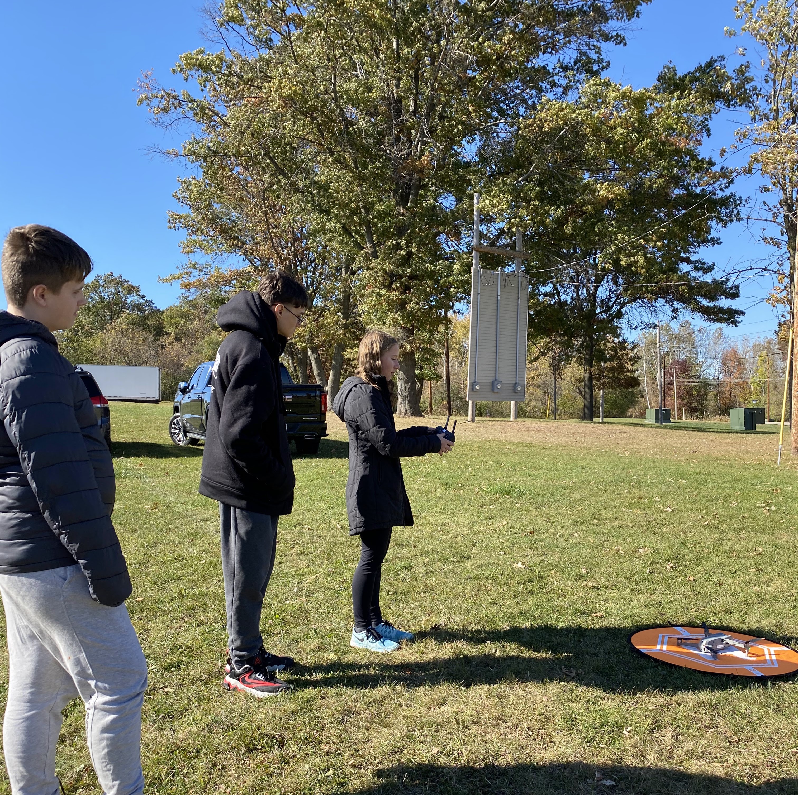 Three students stand near a drone and a landing pad