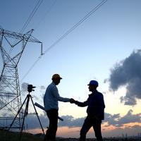 Two engineers shaking hands in front of a power line