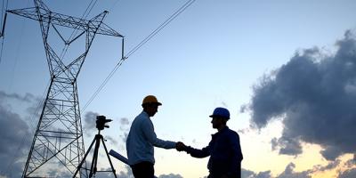 Two engineers shaking hands in front of a power line